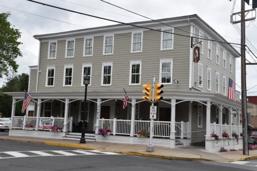 A three-story gray building with a porch, American flags, and flower pots, located at a street intersection.