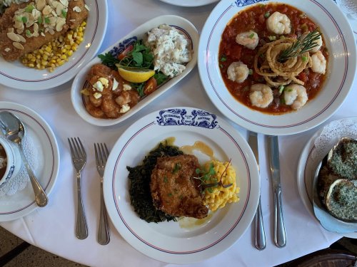A table set with various dishes: fried fish, shrimp, pasta, and sides, all elegantly presented on white plates.