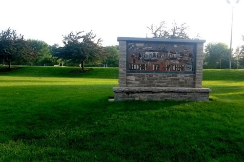 Sign for Deborah Fish Hatchery along a grassy area, surrounded by trees and a clear sky.