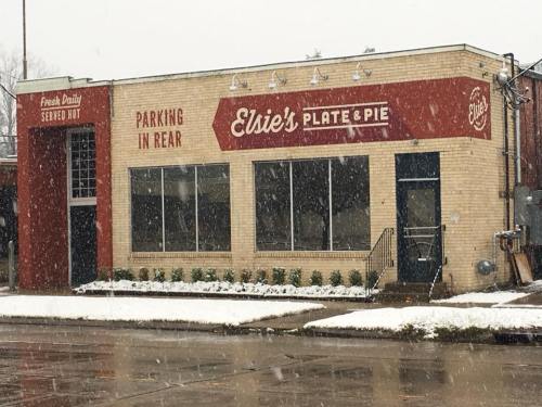 A cozy restaurant, "Elsie's Plate & Pie," with a snowy exterior and a sign indicating parking in the rear.