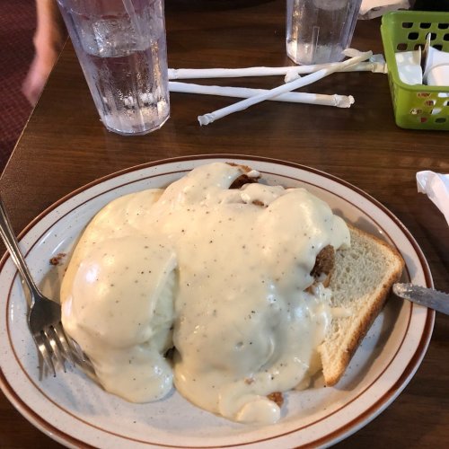 A plate of biscuits and gravy topped with creamy sauce, served with slices of bread, on a wooden table.