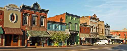 Historic storefronts line a sunny street, showcasing colorful facades and awnings in a charming small town.