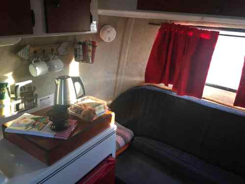 Cozy interior of a camper with a kitchenette, red curtains, and a seating area, featuring a kettle and cookbooks.