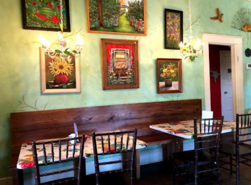 A cozy restaurant interior with green walls, wooden benches, and colorful artwork hanging above tables.