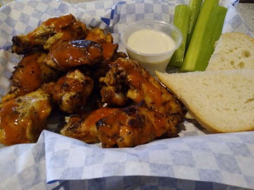 A basket of chicken wings with sauce, celery sticks, a side of ranch dressing, and two slices of bread.