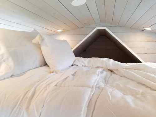 Cozy loft bedroom with white bedding and a sloped ceiling, featuring soft lighting and a minimalist design.