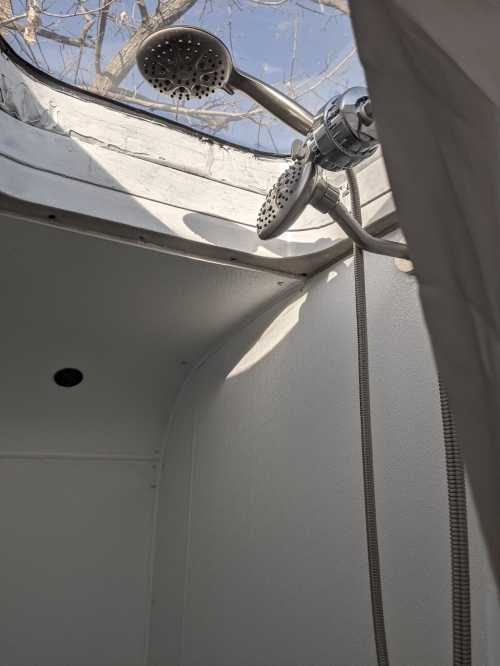 A shower with two showerheads, set in a bright, open space with a view of tree branches outside.