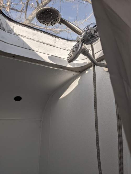 A shower with two showerheads, set in a bright, open space with a view of tree branches outside.