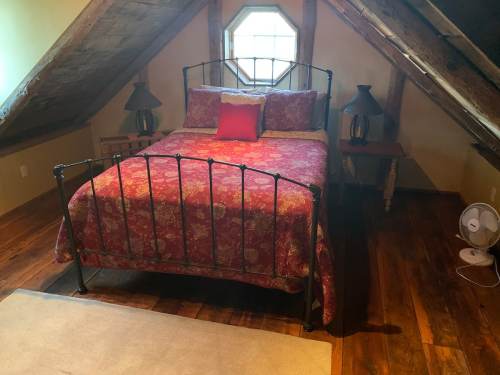 Cozy attic bedroom with a metal bed, floral bedding, two lamps, and a fan on wooden floors.