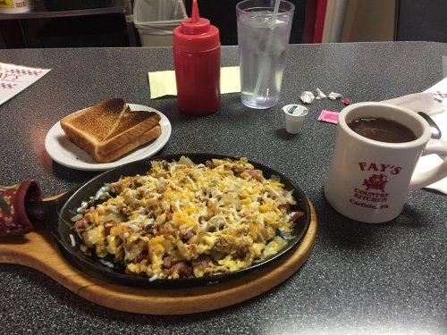 A sizzling plate of breakfast hash with toast, coffee, and condiments on a diner table.