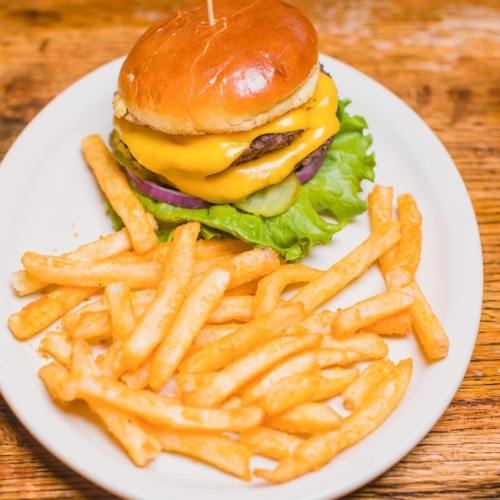 A juicy cheeseburger with lettuce, onion, and pickles, served with a side of golden French fries on a white plate.
