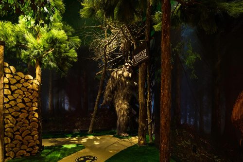 A forest scene featuring tall trees, a sign for "Bigfoot Forest," and a shadowy figure resembling Bigfoot.
