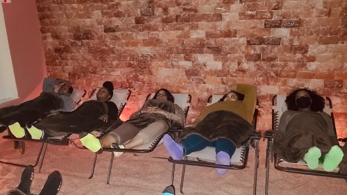 Five people relax on lounge chairs in a spa-like setting, covered with blankets, in a warm, soothing environment.