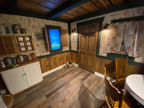 Cozy room with floral wallpaper, wooden accents, a table, chairs, and a window displaying a scenic view.