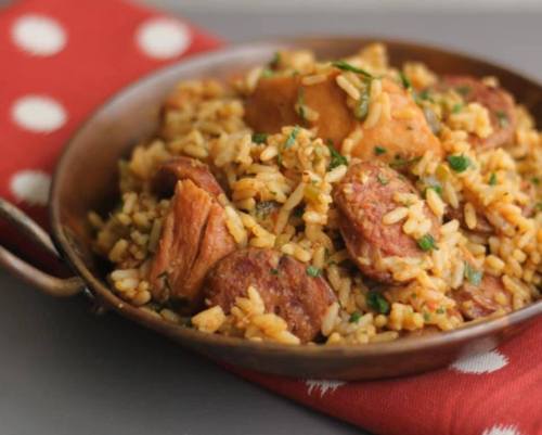 A bowl of flavorful rice mixed with sausage and chicken, garnished with herbs, on a red polka dot napkin.