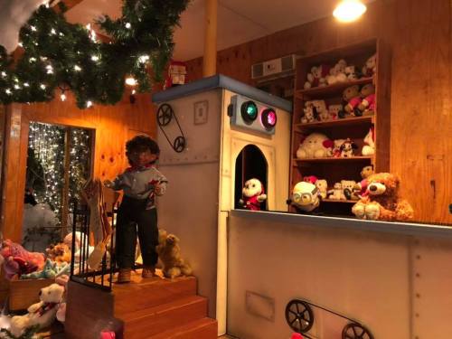 A cozy room decorated with stuffed animals, a doll at the stairs, and colorful lights creating a festive atmosphere.
