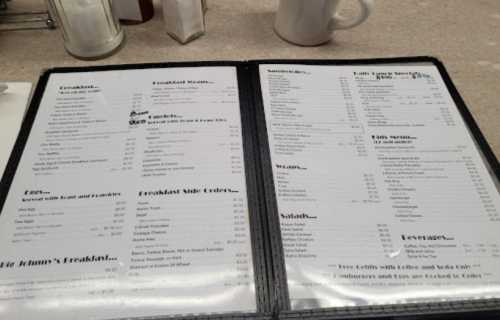 A diner menu featuring breakfast items, sandwiches, salads, and beverages, displayed on a black folder.