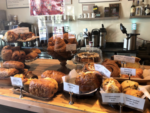A display of various baked goods, including croissants, pastries, and cakes, with price tags on a wooden counter.