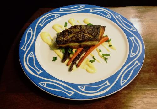 A beautifully plated fish dish with roasted carrots and a creamy sauce, garnished with herbs on a decorative plate.