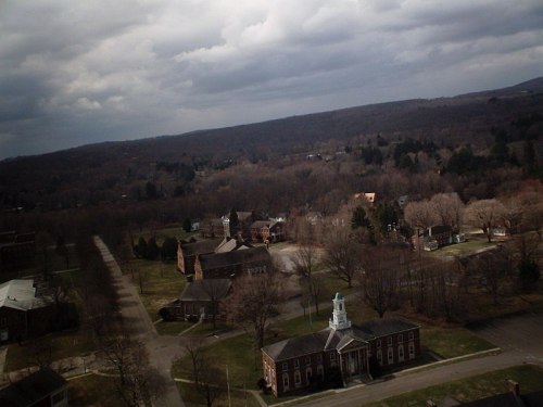 Aerial view of a quiet, wooded area with buildings and a church, under a cloudy sky.