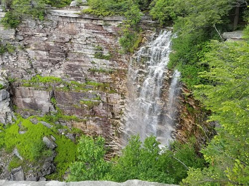 A cascading waterfall flows down rocky cliffs, surrounded by lush green foliage and trees.