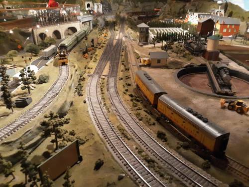 A detailed model train layout featuring tracks, trains, buildings, and scenic elements in a miniature landscape.