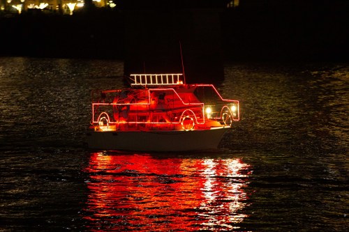 A brightly lit boat with red lights glides across dark water, reflecting its glow in the surface.