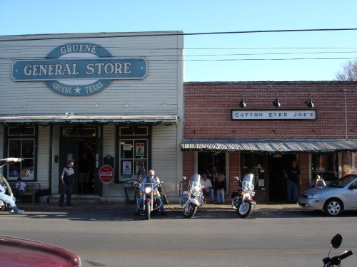 A street view of Gruene, Texas, featuring the General Store and Cotton Eyed Joe's, with parked motorcycles in front.