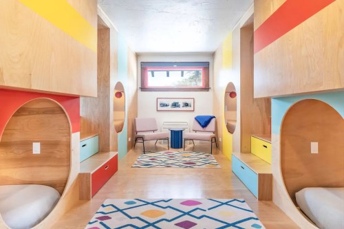 Brightly colored room with circular nooks, wooden walls, and cozy seating, featuring a playful rug and modern decor.