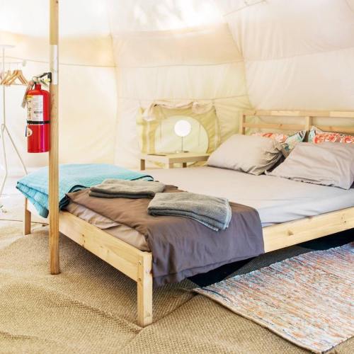 Cozy tent interior with a wooden bed, colorful bedding, a lamp, and a fire extinguisher on the side.