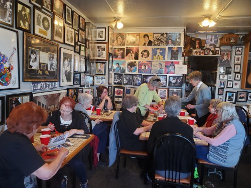 A group of seniors gathers around tables in a cozy room filled with music memorabilia and framed photos.