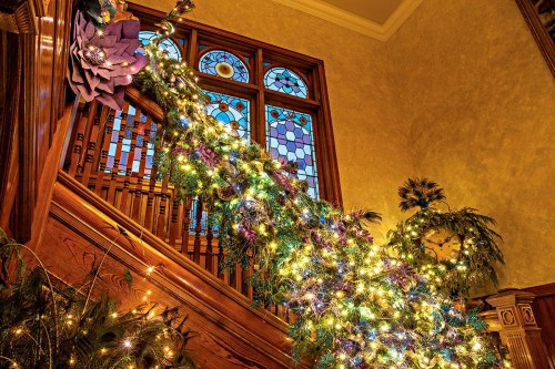 A beautifully decorated staircase with colorful lights and greenery, featuring stained glass windows in the background.
