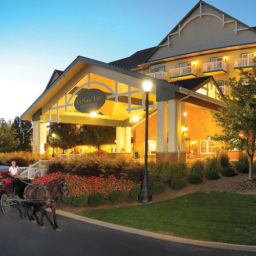 A horse-drawn carriage approaches the entrance of Carlisle Inn, surrounded by flowers and warm evening lights.