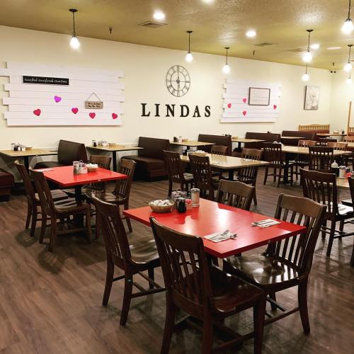 Interior of a cozy restaurant with wooden tables and chairs, decorated with hearts and a sign that reads "LINDAS."