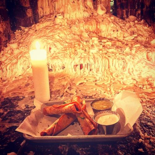 A plate with two crispy tacos and dipping sauces, illuminated by a candle against a backdrop of melted wax.