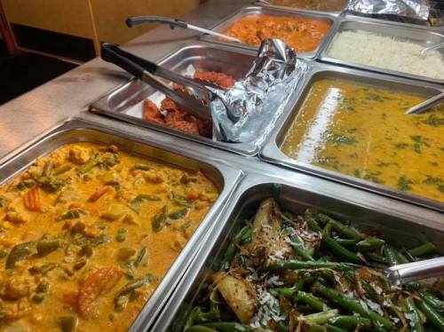 A variety of colorful dishes in metal trays, including curry, rice, and vegetables, with serving utensils.