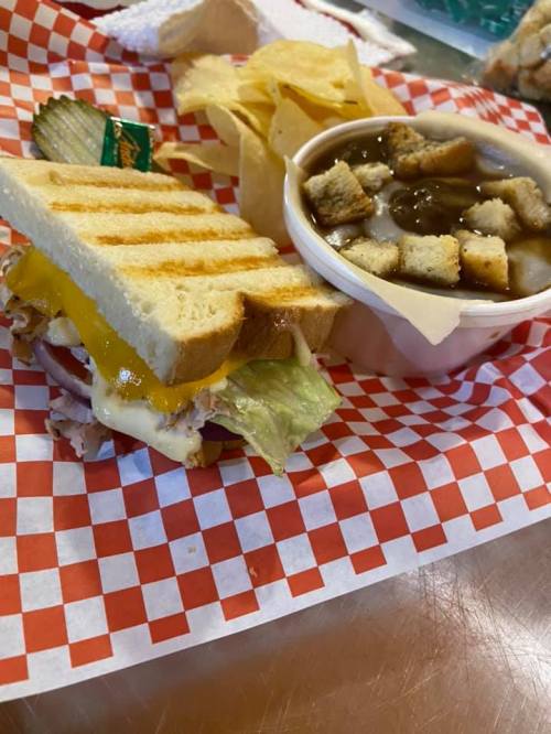 A grilled sandwich with cheese, lettuce, and turkey, served with chips and a bowl of soup topped with croutons.