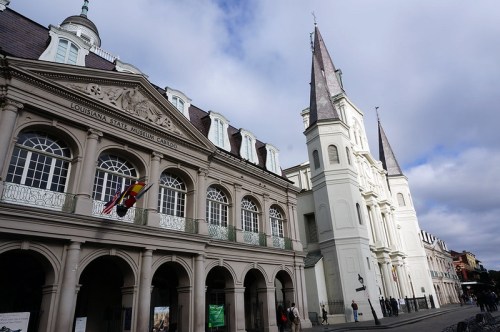Historic buildings in New Orleans, featuring ornate architecture and a tall church steeple against a cloudy sky.