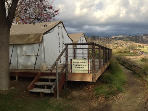 Tents with a wooden deck labeled "Reserved for Roar & Snore Campers" in a scenic outdoor setting.