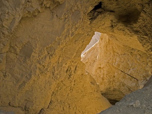 A view of a rocky cave with a bright opening at the top, showcasing textured yellowish walls.