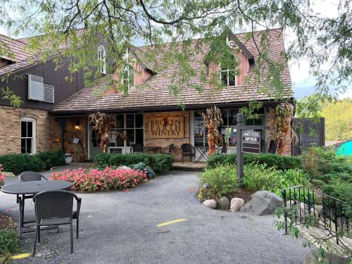 A charming winery building with a sign, surrounded by flowers and outdoor seating.