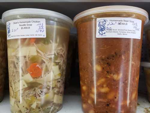 Two large containers of homemade soups: chicken noodle and bean soup, labeled with prices and ingredients.