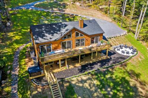 Aerial view of a wooden house with a deck, surrounded by trees and a landscaped yard.