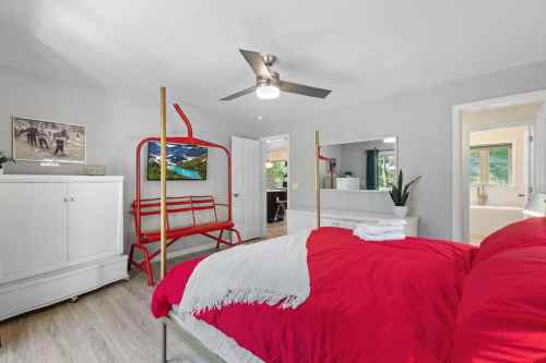 Bright bedroom featuring a red bed, modern ceiling fan, and stylish decor with a view of greenery outside.