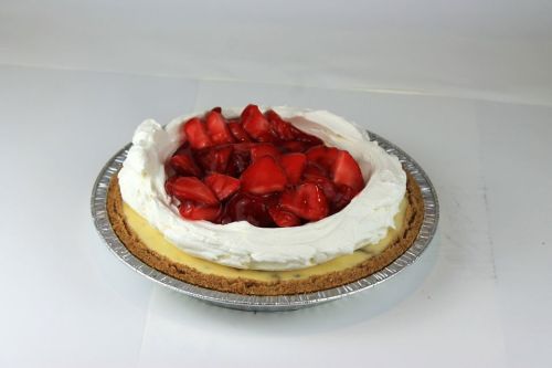 A creamy pie with a graham cracker crust, topped with whipped cream and fresh strawberries.