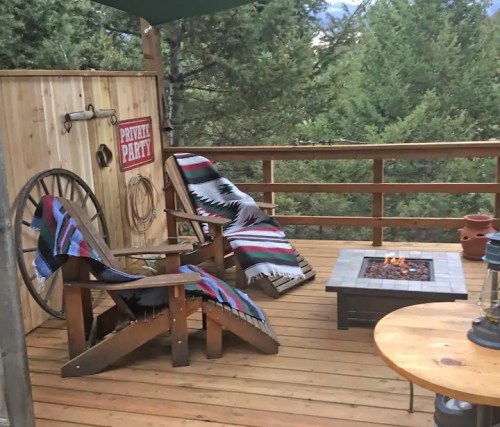 Cozy outdoor deck with two chairs, a fire pit, and a "Private Party" sign, surrounded by trees.