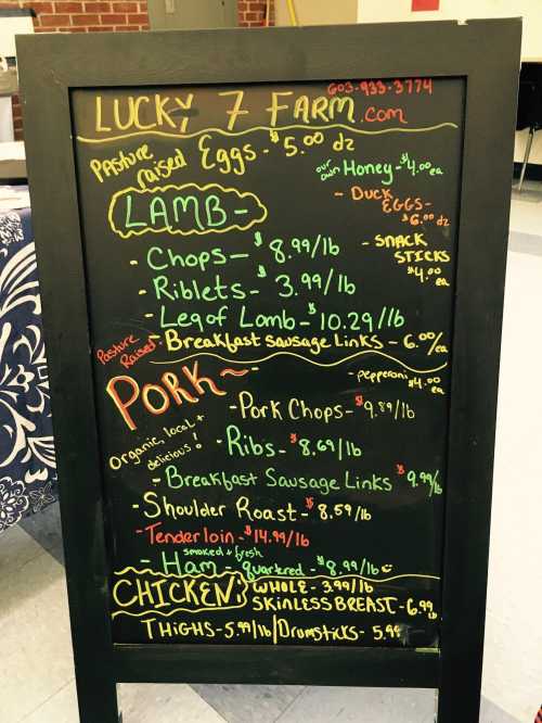 Chalkboard menu listing prices for farm products: lamb, pork, and chicken, including various cuts and items.