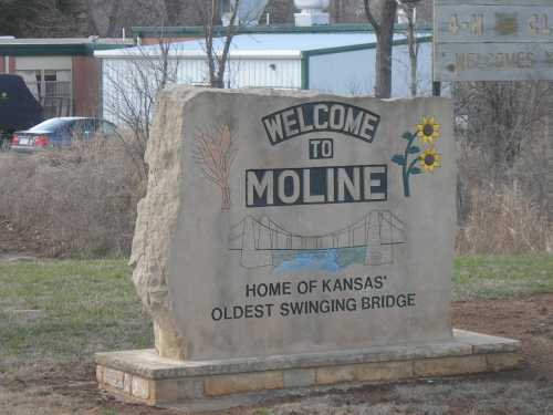 Welcome sign for Moline, Kansas, featuring a drawing of a bridge and sunflowers, highlighting the town's historic swinging bridge.