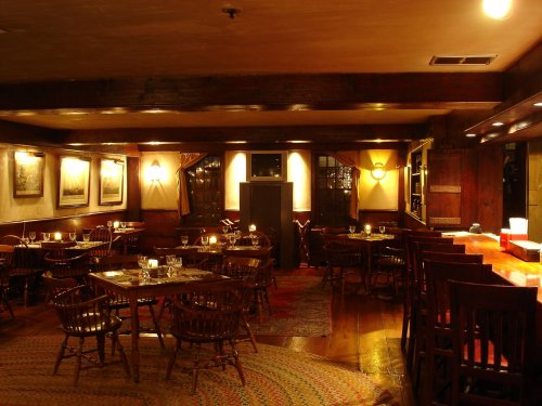 Cozy restaurant interior with wooden tables, chairs, warm lighting, and artwork on the walls.