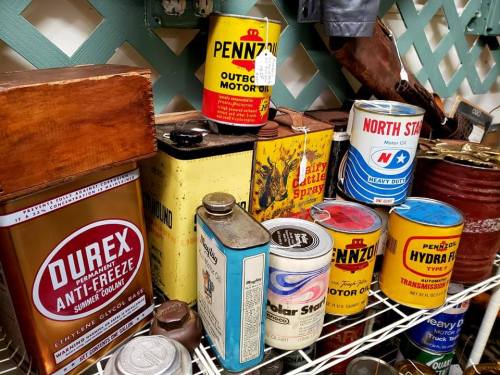 A collection of vintage cans and containers, including motor oil and anti-freeze, displayed on a shelf.